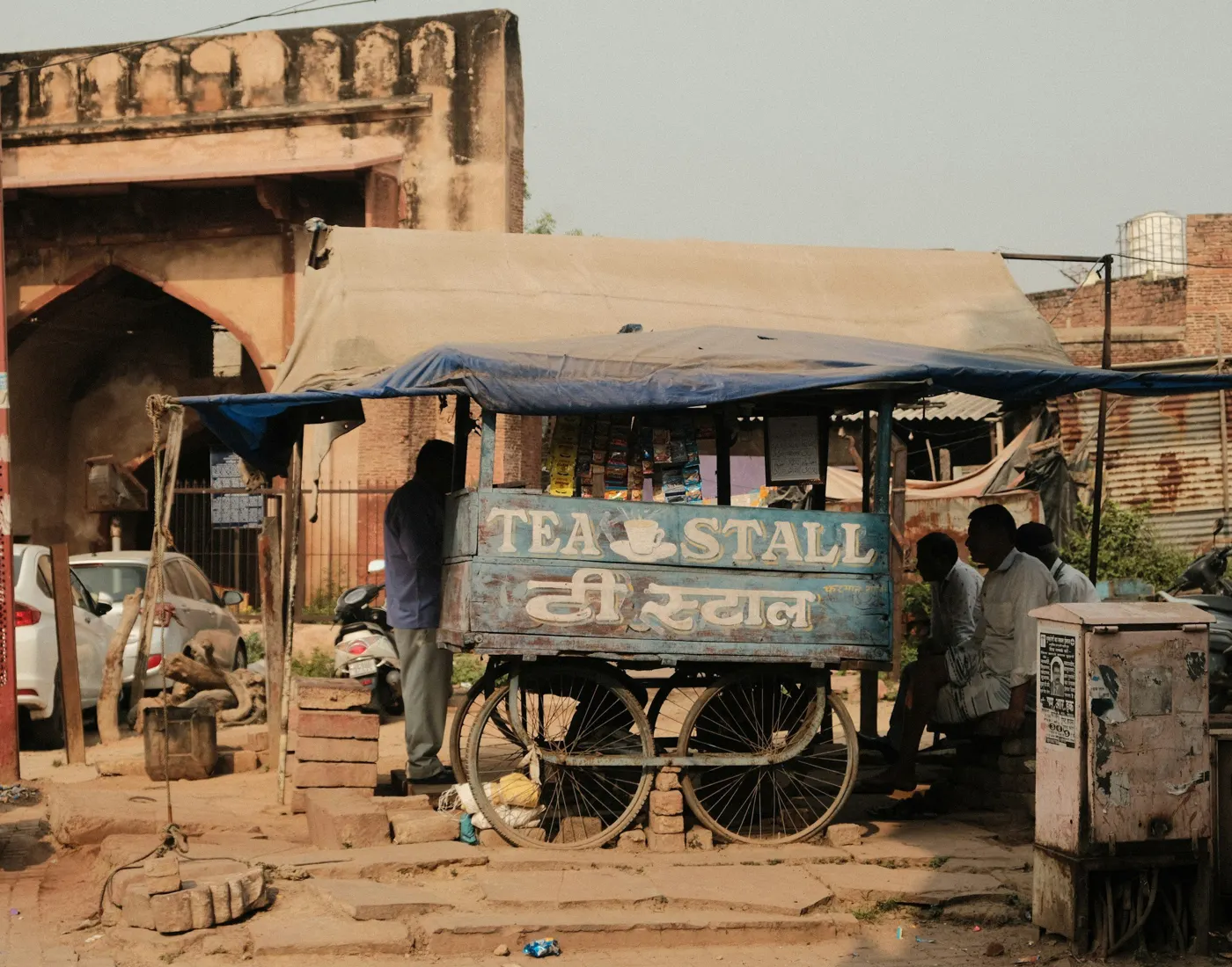 A roadside tea stall cart with people sitting in its shade